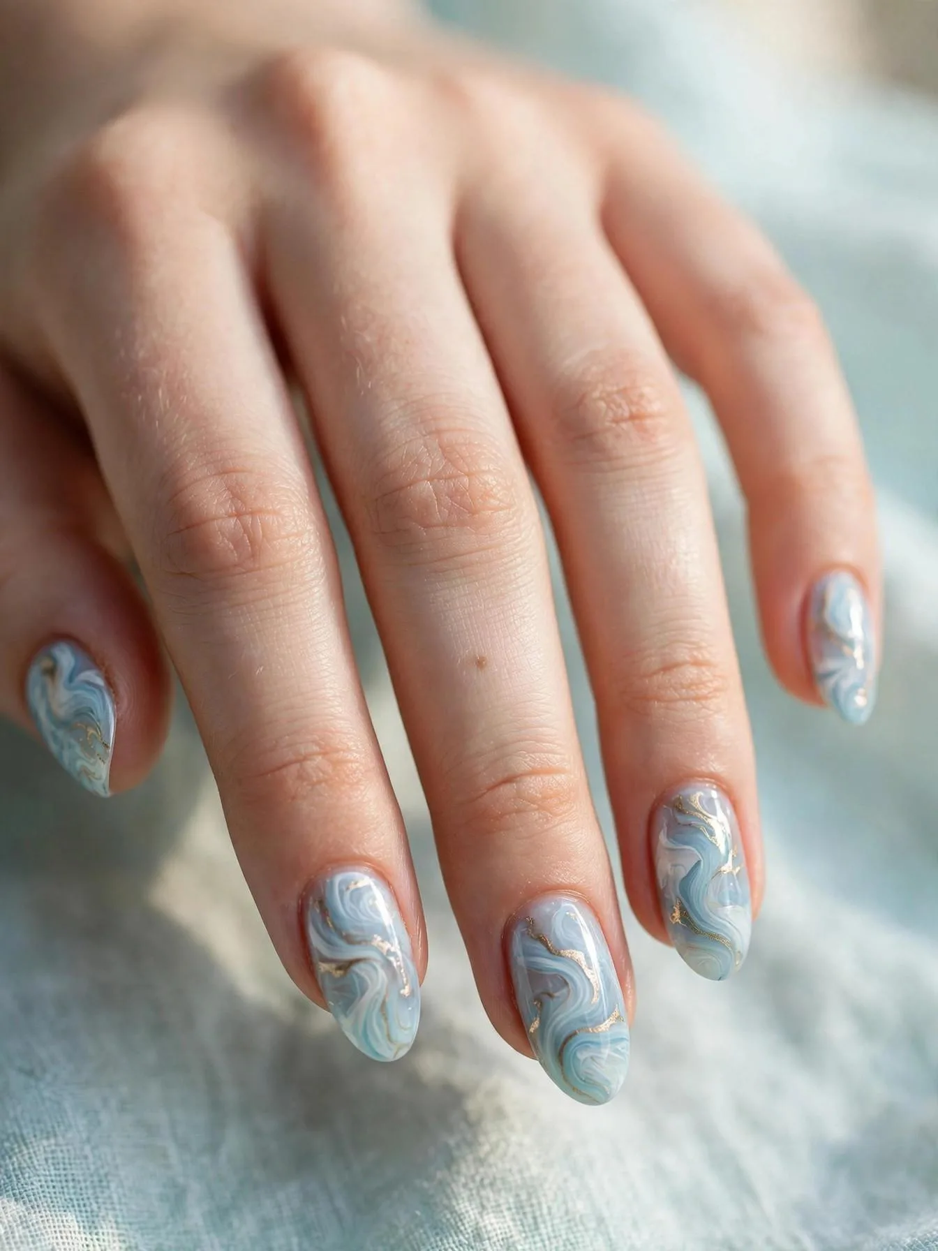Medium almond nails with airy light blue, gold, and white summer marbling.