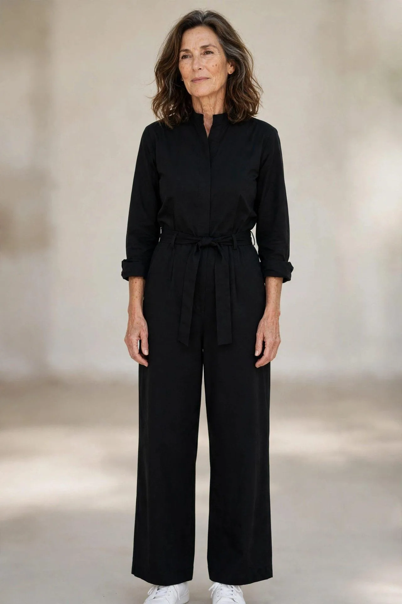 Mature lady in sleek black one-piece jumpsuit with minimalist white sneakers