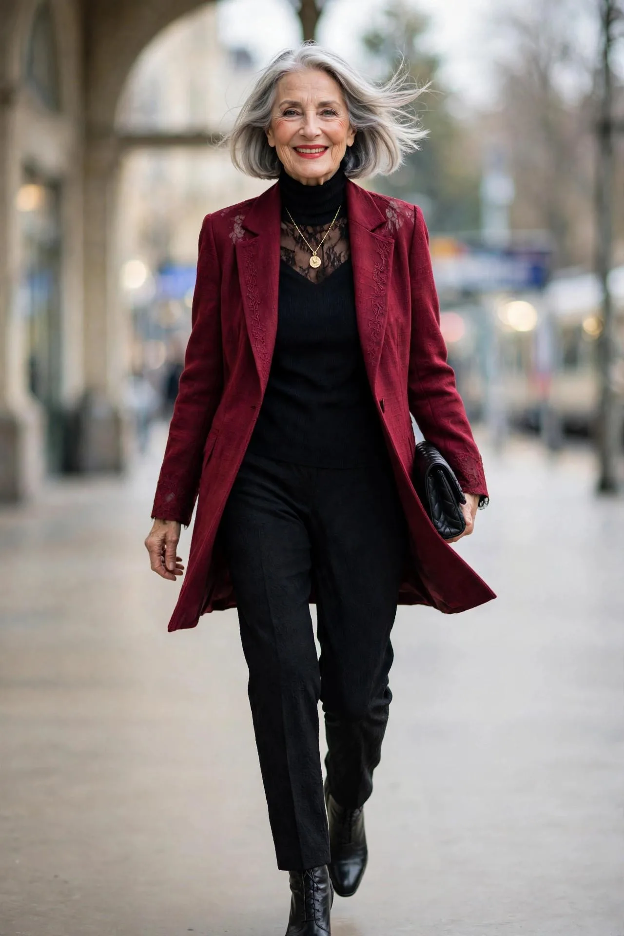 Festive mature woman wearing cranberry blazer over black turtleneck and trousers with gold pendant.