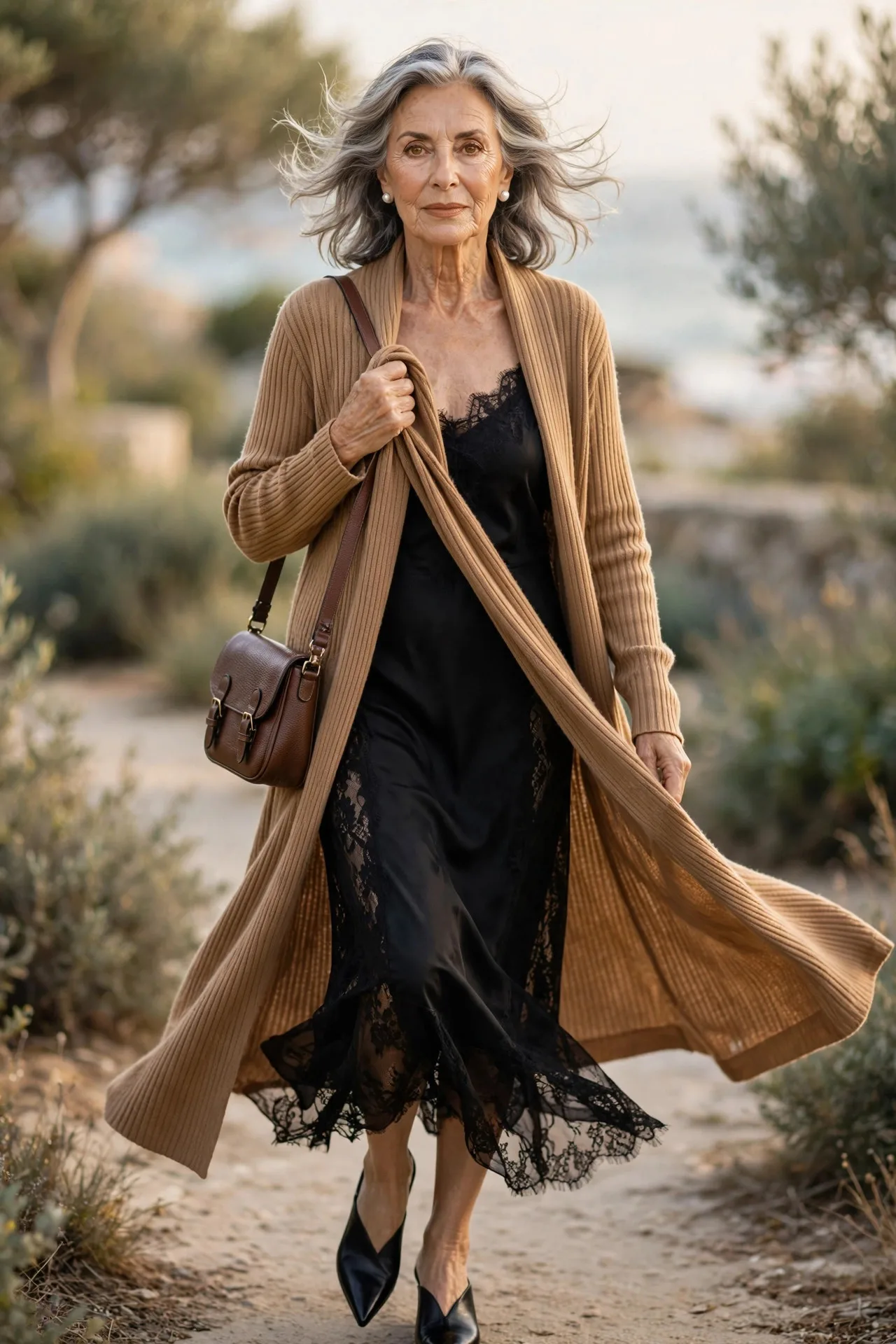 Duster Confidence — A long ribbed camel duster cardigan worn open over a black bias-cut slip midi dress, with elegant pointed mules and pearl earrings.