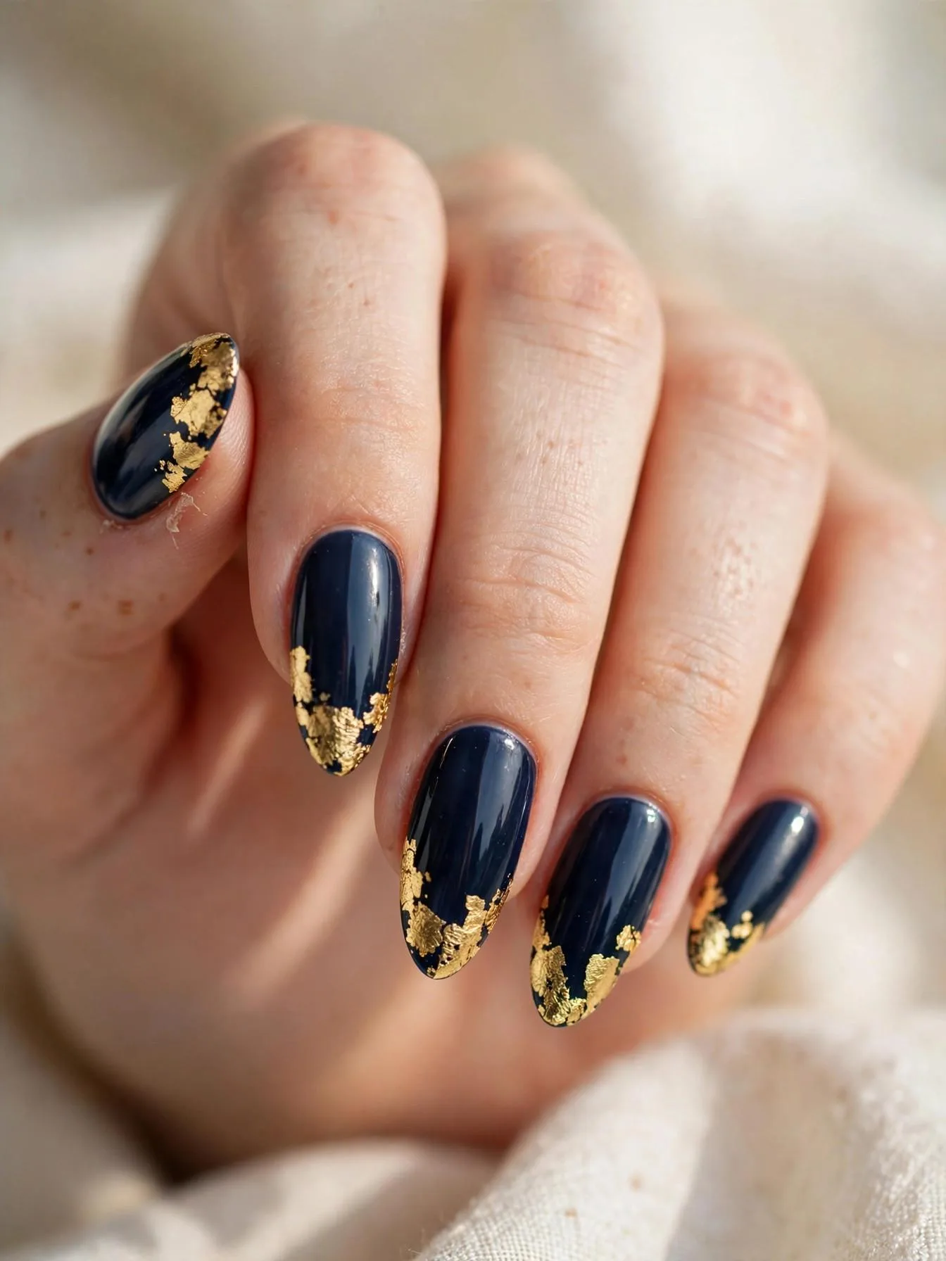 Long almond nails in navy gloss with bold irregular gold leaf tips.