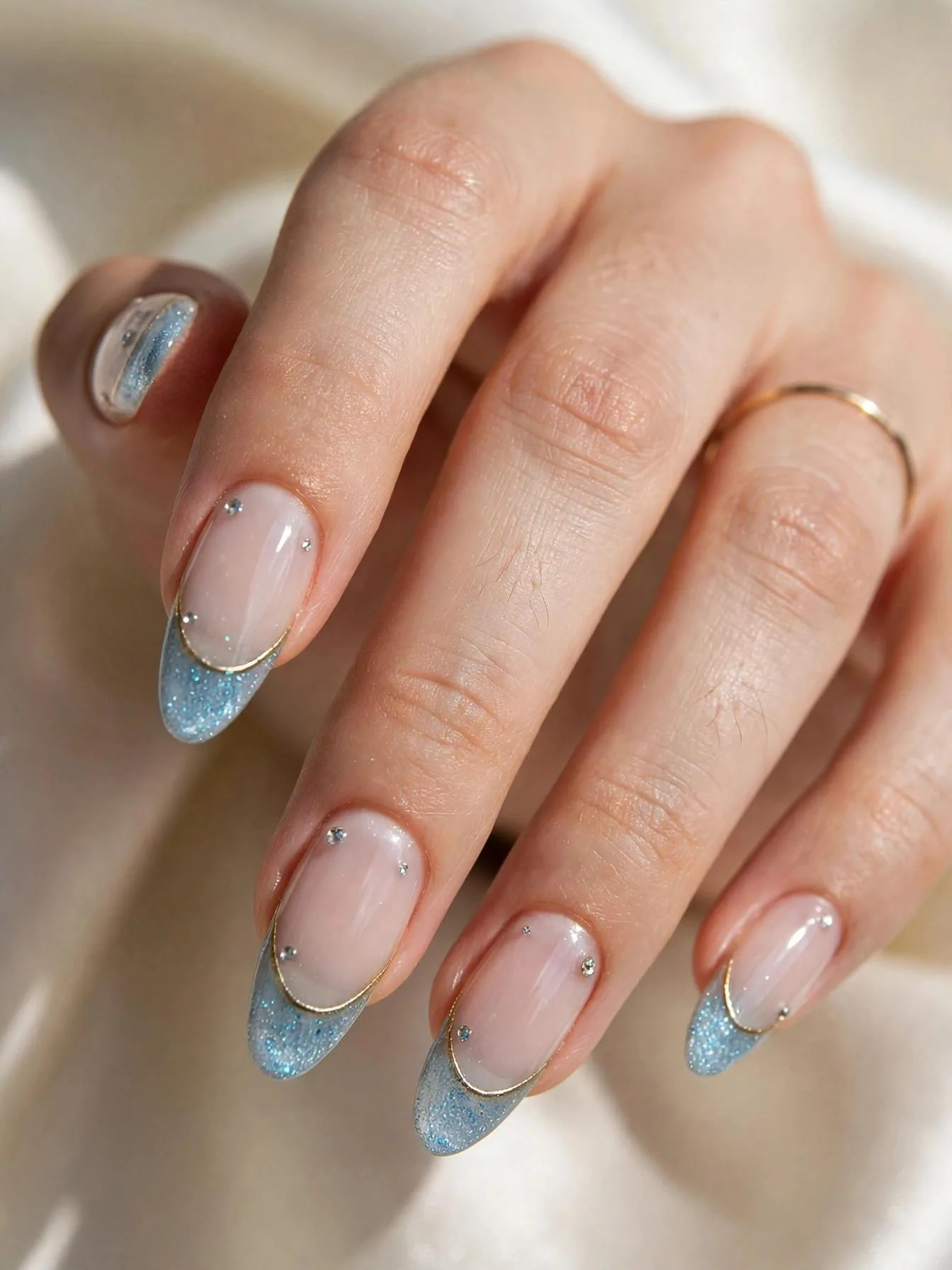 Long almond nails with icy blue glitter French tips, gold chrome outline, rhinestones.