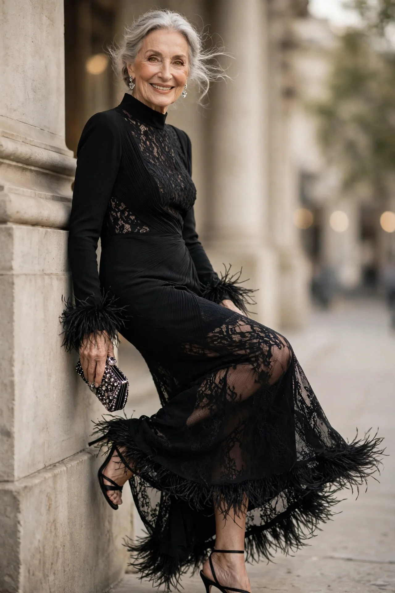 Feathered Midnight Finale — A black crepe column evening gown with long sleeves, a high neckline and dramatic black feather trim at the cuffs and hem, worn with black satin strappy heels.