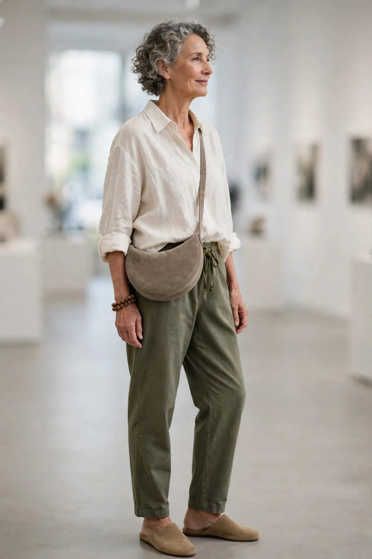 Mature lady modeling a contemporary half-moon suede shoulder bag in warm taupe at an exhibition.