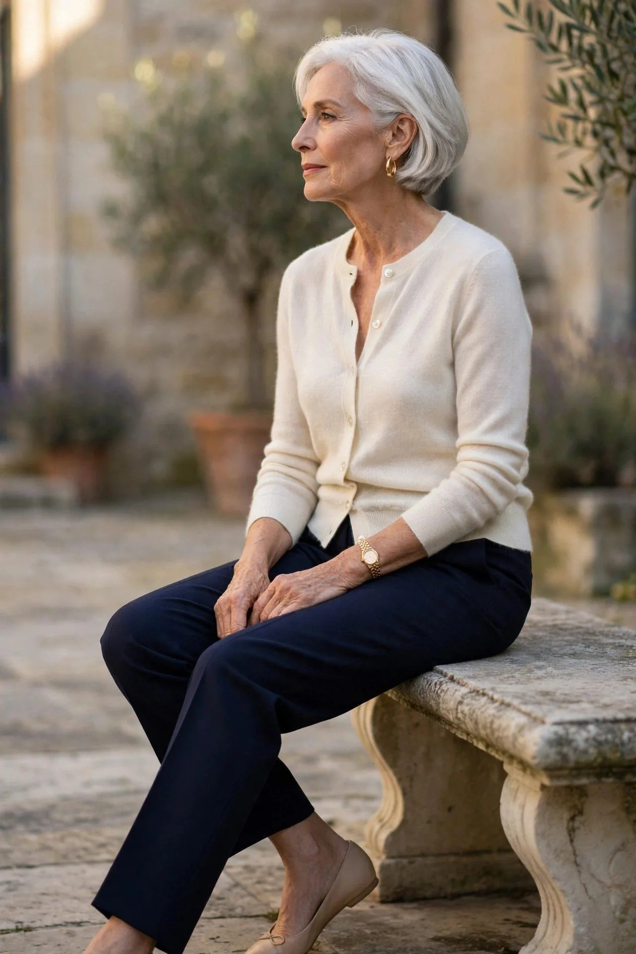 Graceful senior lady sitting comfortably in midnight blue tailored pants and an ivory cashmere cardigan styled as a blouse, easy opulence.