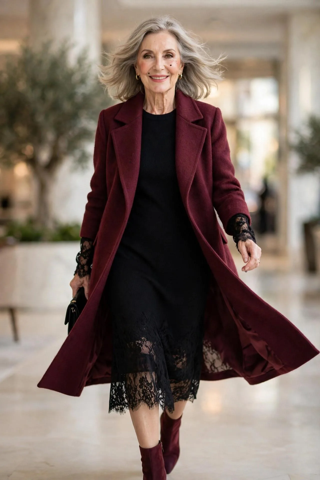 Glowing mature woman in wine cashmere coat over black knit midi dress with heeled boots.