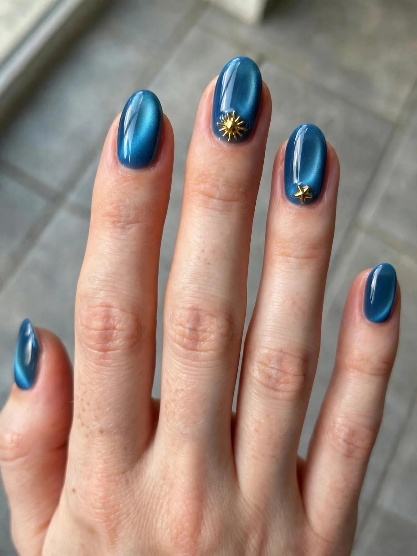Short almond nails with blue aura cat eye glow and 3D gold star charms.