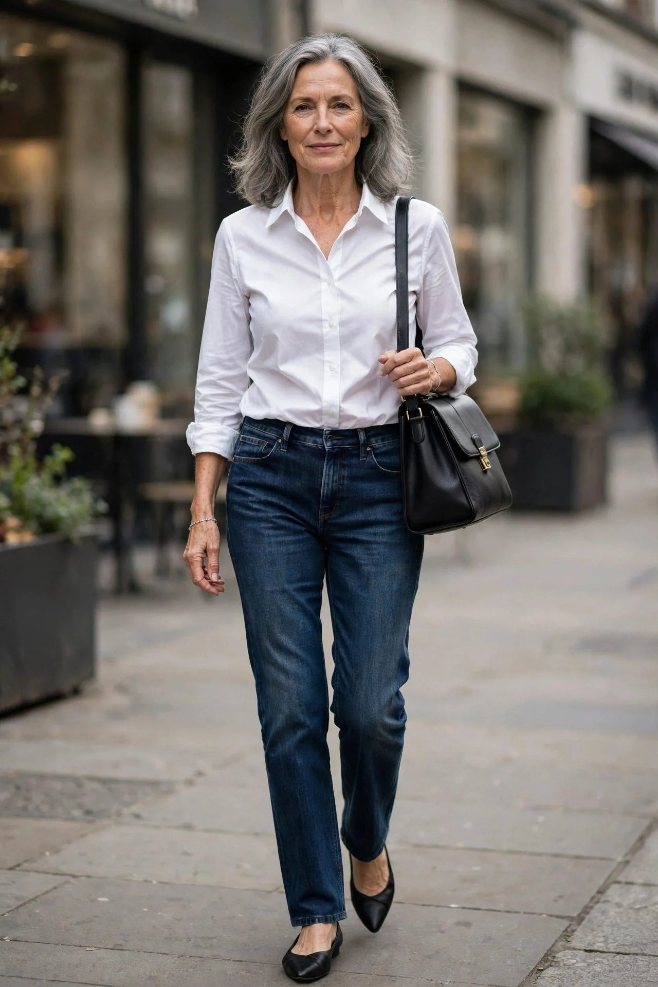 Graceful lady past fifty in denim and white blouse with a timeless black leather shoulder purse downtown.
