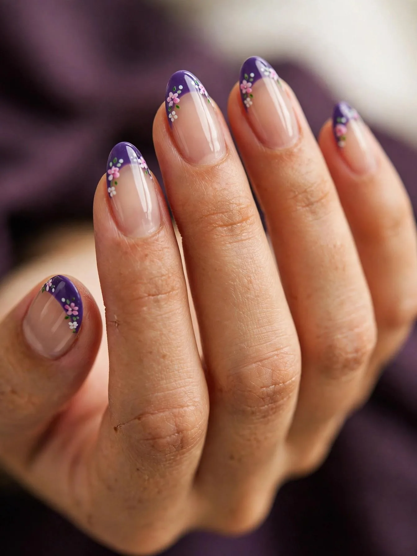 Medium almond nails with violet French tips and tiny floral motifs.