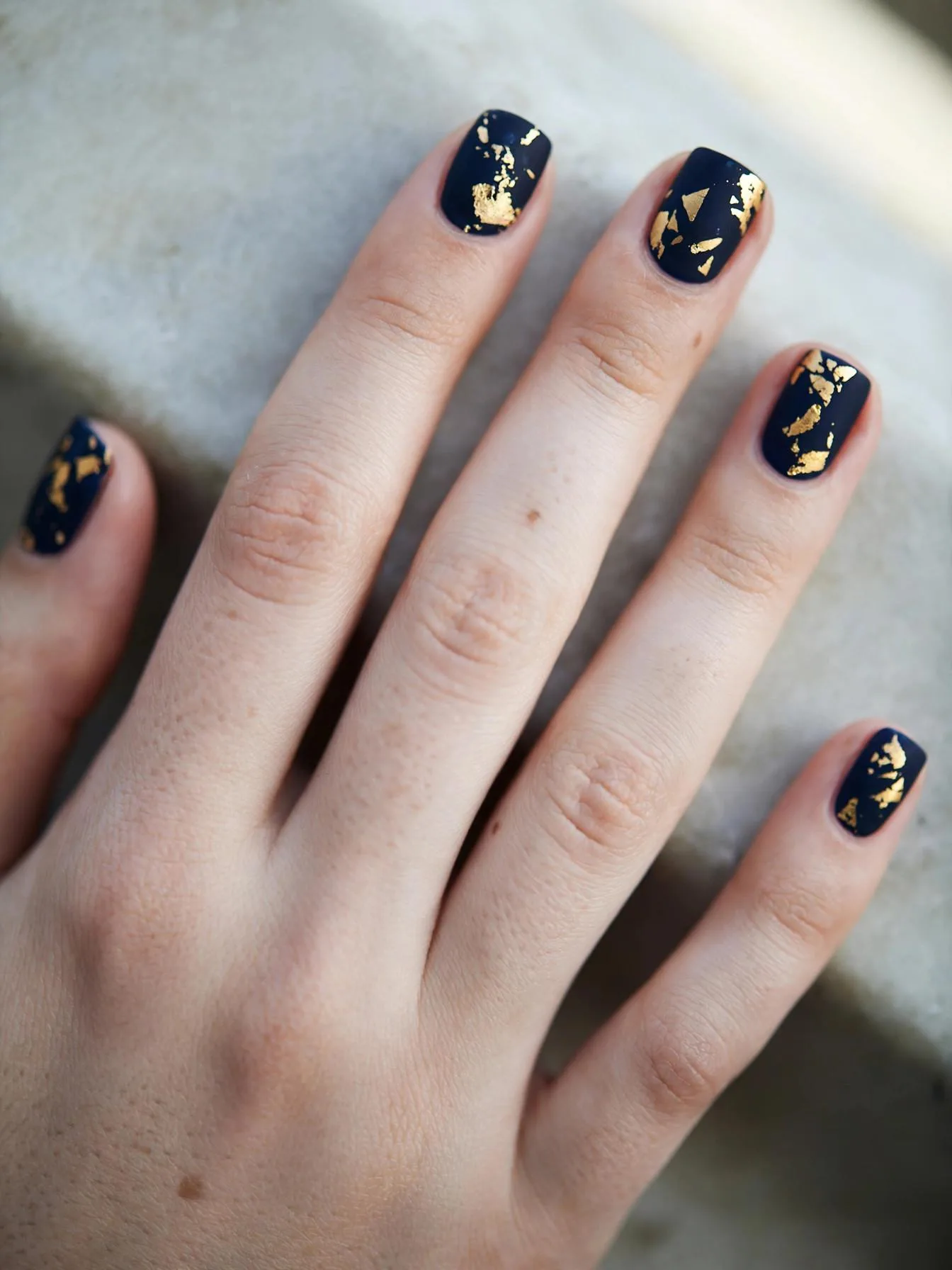 Short square nails in matte midnight navy with irregular gold foil flakes.